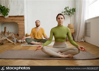 Young family couple practicing meditation sitting in lotus position. Morning yoga in pair, mindfulness exercise for wellness and relaxation. Young family couple practicing meditation sitting in lotus position