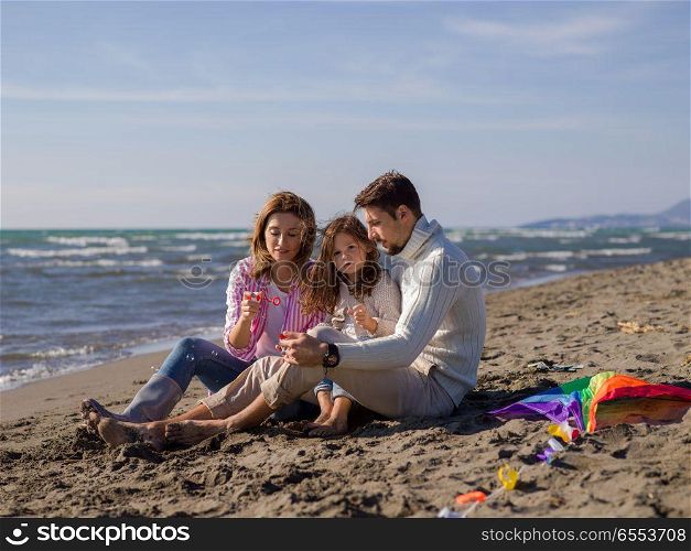 Young family enjoying vecation during autumn day. Family with little daughter resting and having fun making soap bubble at beach during autumn day