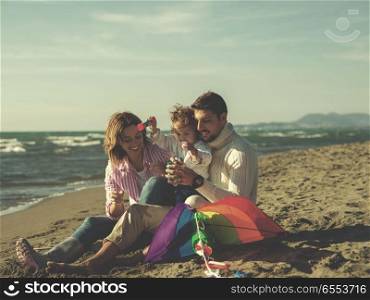 Young family enjoying vecation during autumn day. Family with little daughter resting and having fun making soap bubble at beach during autumn day colored filter