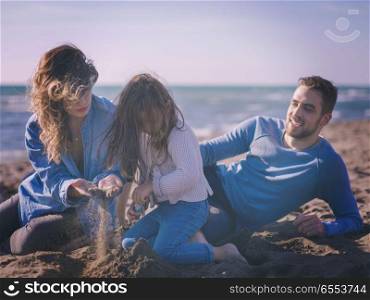 Young family enjoying vecation during autumn day. Family with little daughter resting and having fun at beach during autumn day colored filter