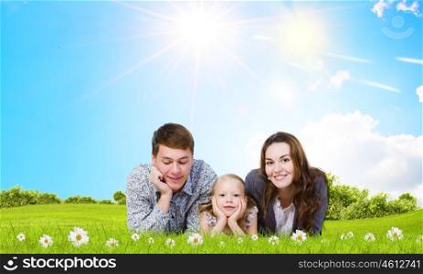 Young family. Happy family of three lying on green grass