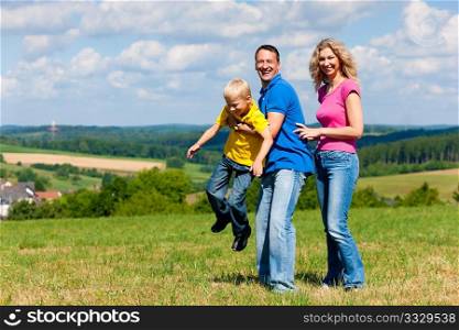 Young family having a walk in the sun over the meadow on a bright summer day and making jokes