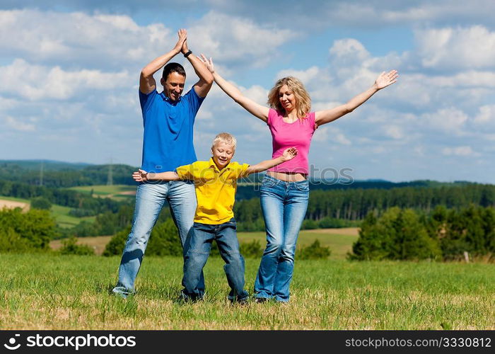 Young family having a walk in the sun over the meadow on a bright summer day and making jokes