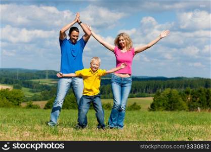 Young family having a walk in the sun over the meadow on a bright summer day and making jokes
