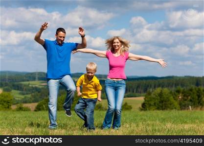 Young family having a walk in the sun over the meadow on a bright summer day