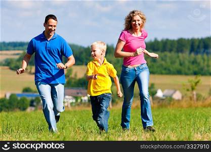 Young family having fun in the sun playing tag on the meadow an a bright summer day