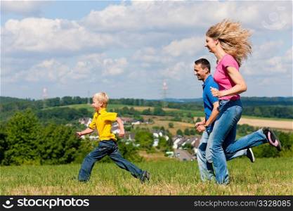 Young family having fun in the sun playing tag on the meadow an a bright summer day