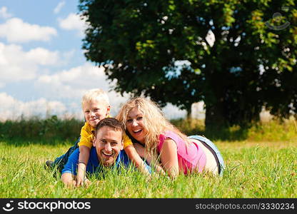 Young family having fun in the sun playing tag on the meadow an a bright summer day