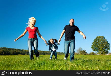 Young family having fun in the sun running over the meadow an a bright summer day