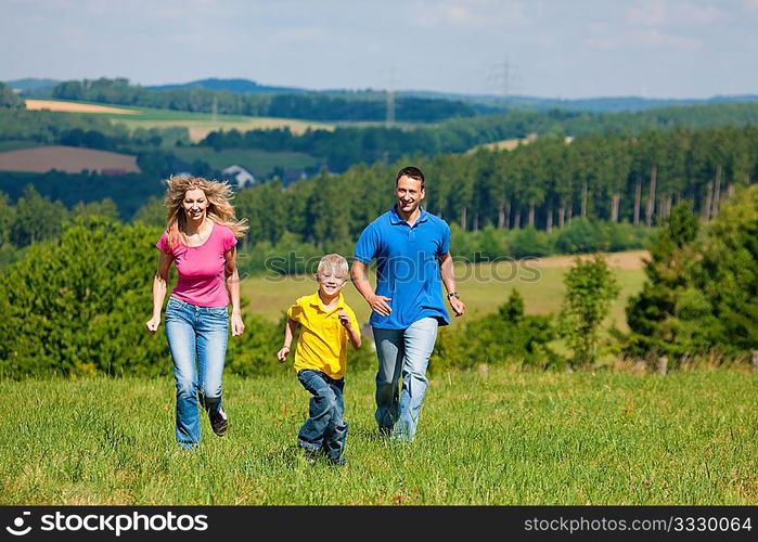 Young family having fun in the sun running over the meadow an a bright summer day