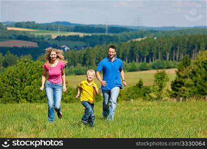 Young family having fun in the sun running over the meadow an a bright summer day