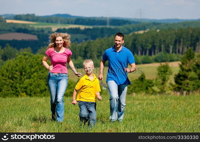 Young family having fun in the sun running over the meadow an a bright summer day