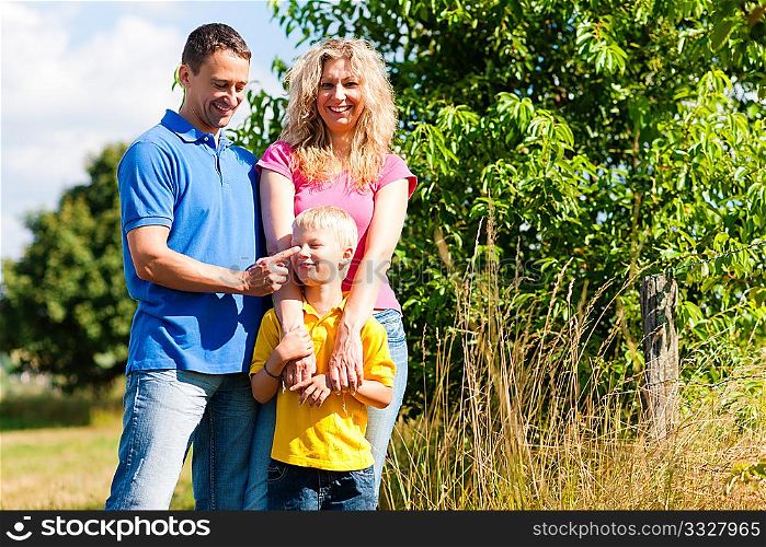 Young family having fun in the sun standing on the meadow an a bright summer day