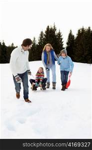 Young Family In Alpine Snow Scene With Sled