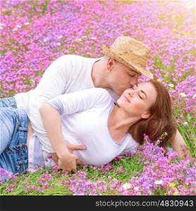 Young family kissing in the garden, lying down on spring floral field in warm sunny day, gentle feelings, happy lifestyle, love concept&#xA;