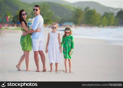 Young family of four on beach vacation. Family of four walking on white beach
