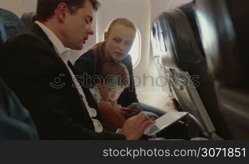 Young family of three traveling by air. Father busy with touch pad and talking to the wife, child using smart phone
