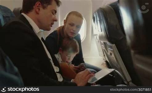 Young family of three traveling by air. Father busy with touch pad and talking to the wife, child using smart phone