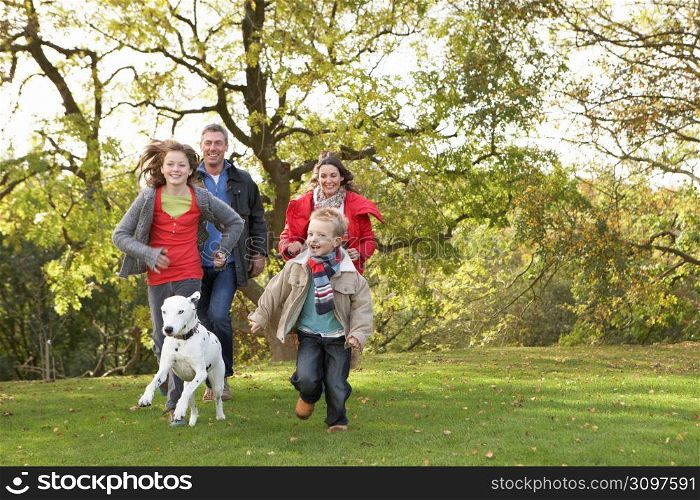 Young Family Outdoors Walking Through Park With Dog