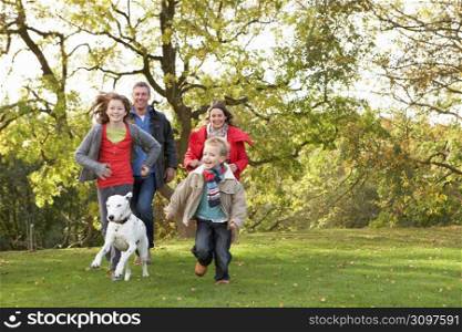 Young Family Outdoors Walking Through Park With Dog