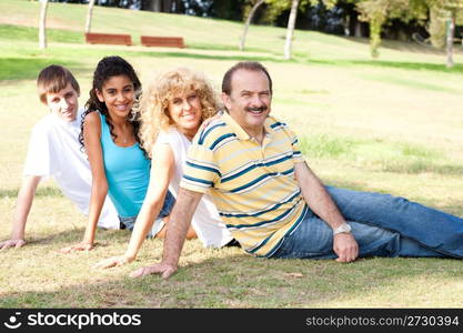 Young family relaxing in park and smiling at camera.