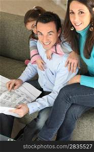 Young family relaxing on sofa with newspaper