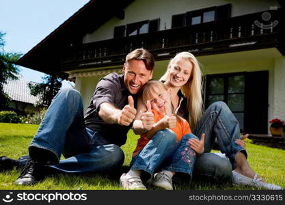 Young family sitting in the sun on the lawn in front of their new home - a single house