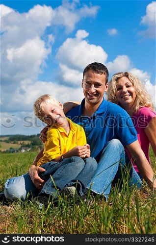Young family sitting in the sun on the meadow an a bright summer day
