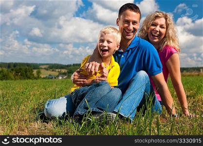 Young family sitting in the sun on the meadow an a bright summer day
