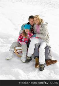 Young Family Sitting On A Sled In The Snow
