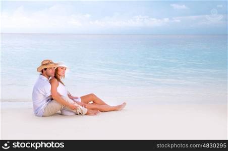 Young family spending summer vacation on romantic beach resort, sitting and hugging on seashore, looking away, affection concept
