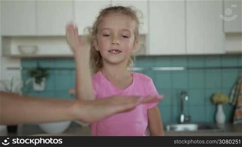 Young family stacking hands on top of each other symbolizing unity against domestic interior. Attractive parents and smiling curly little daughter making pile of hands in kitchen in the morning. Slow motion.