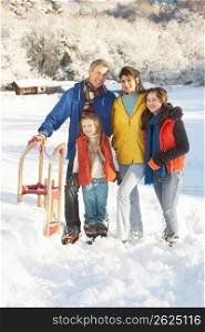 Young Family Standing In Snowy Landscape Holding Sledge