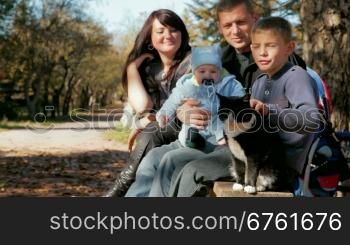 Young family with a toddler and a pet resting on a bench in the park