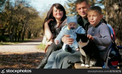Young family with a toddler and a pet resting on a bench in the park