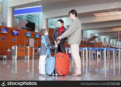 young family with boy standing in airport hall with suitcases side view