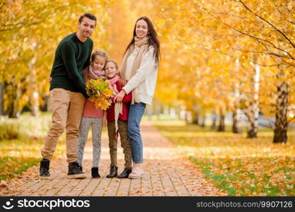 Young family with cute little kids in autumn park on sunny day. Portrait of happy family of four in autumn day. Portrait of happy family of four in autumn day