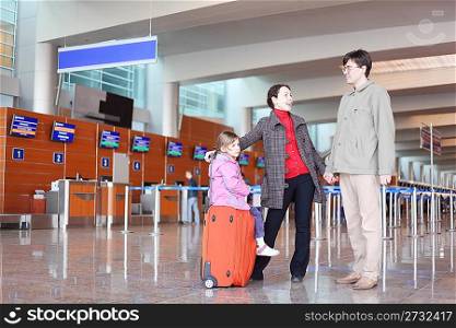 young family with red suitcase standing in airport hall