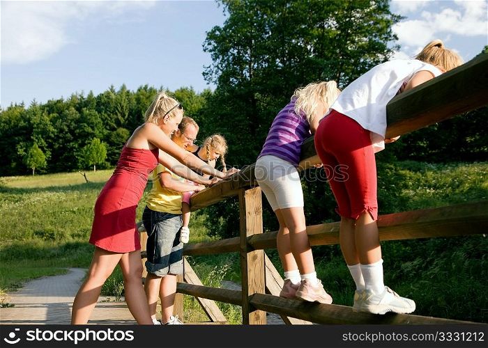 Young family with three children standing on a bridge in the sunlight, focus on girl in front