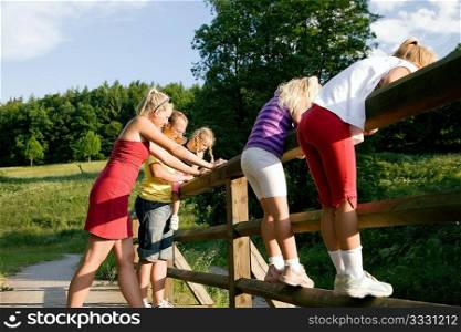 Young family with three children standing on a bridge in the sunlight, focus on girl in front