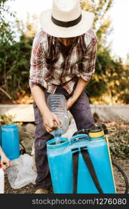 Young farmer preparing organic fertilizer with manual pump tank wearing an old hat and plaid shirt