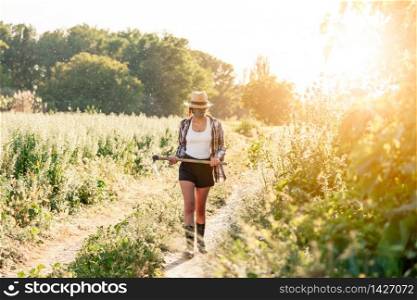 Young farmer woman walking with straw hat surgical mask and hoe