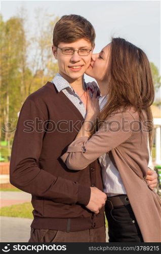 Young fashion elegant stylish couple in love posing in a European city park. Cute girl kisses a hipster man.