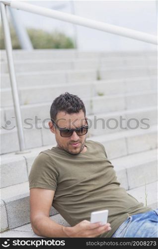 Young fashion man sitting on the steps while using a mobile phone