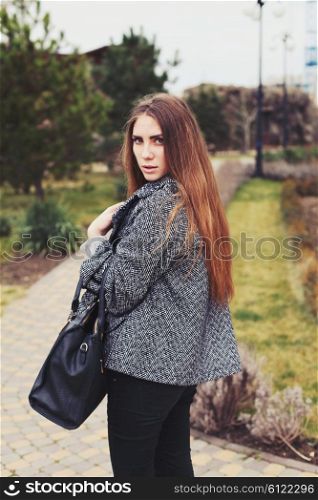 Young fashion sensual woman in warm gray coat with leather bag posing outdoor