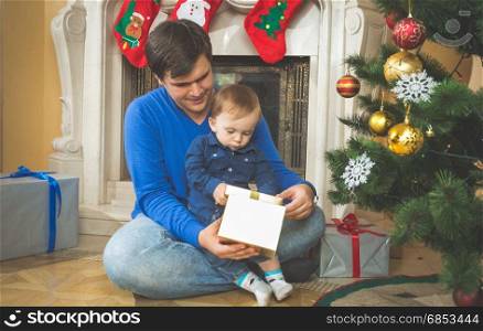 Young father and cute baby son opening Christmas gifts on floor