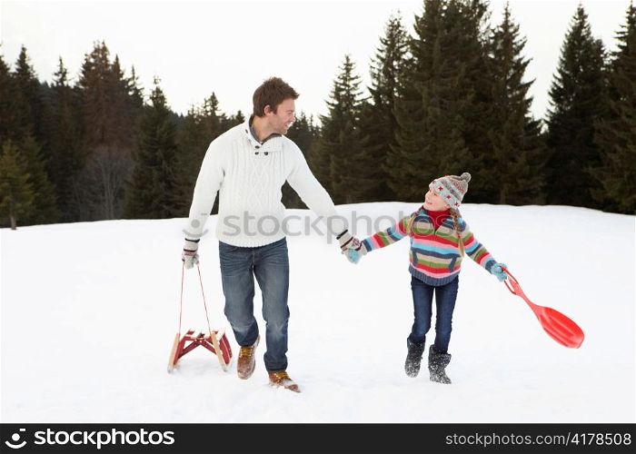 Young Father And Daughter Walking In Snow With Sleds