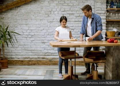 Young father and his cute daughter making dough at rustic home kitchen