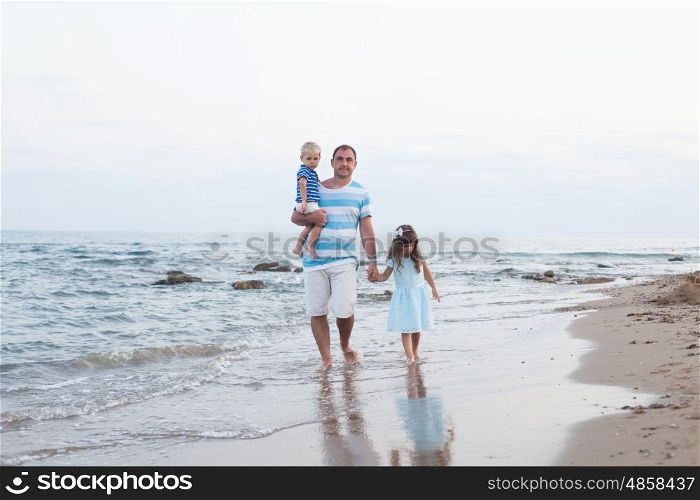 Young father and his two pretty kids walking along sand beach at evening time. Walking on the empty beach
