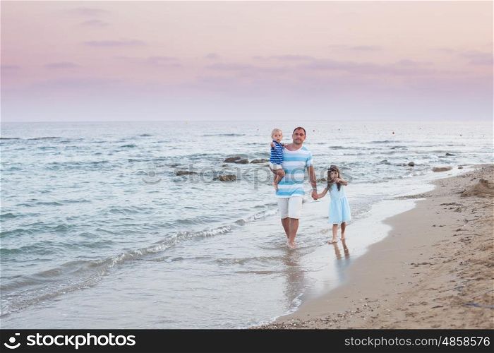 Young father and his two pretty kids walking along sand beach at evening time. Walking on the empty beach